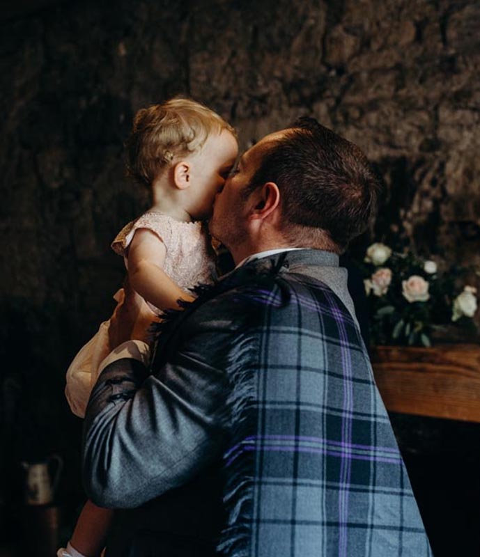 A man in a fly plaid on his wedding day holds a young child affectionately