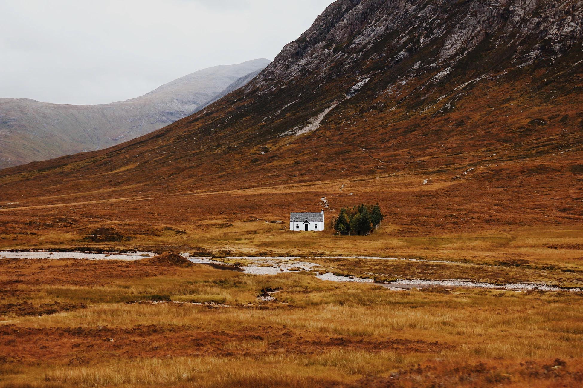 White Bothy home in the North of Scotland with sprawling red hills on an overcast day