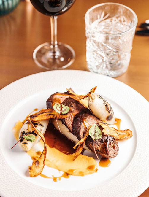 A dish displayed with four slices of tender beef, with charred shallots and garnish