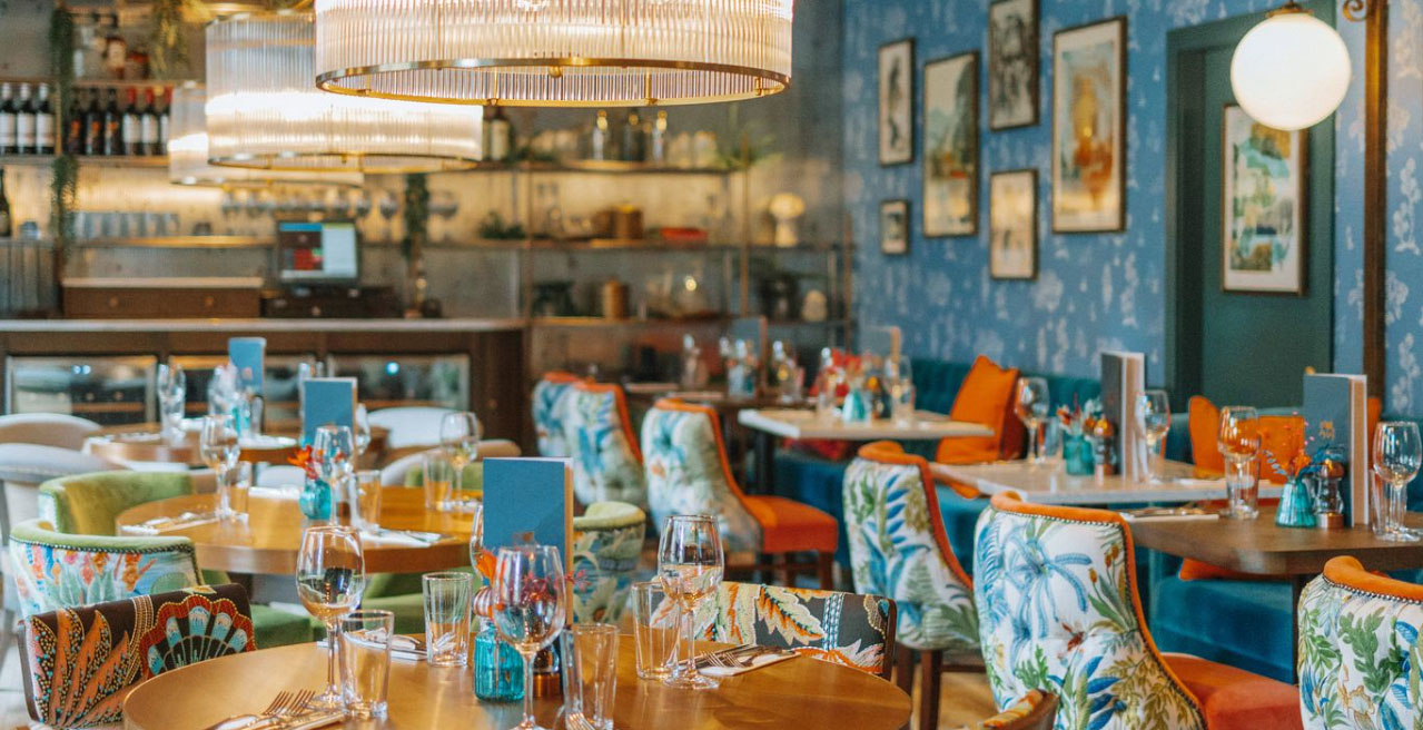 Interiors with blue and orange design, blue wallpaper, framed art on the walls and tables set up for dining
